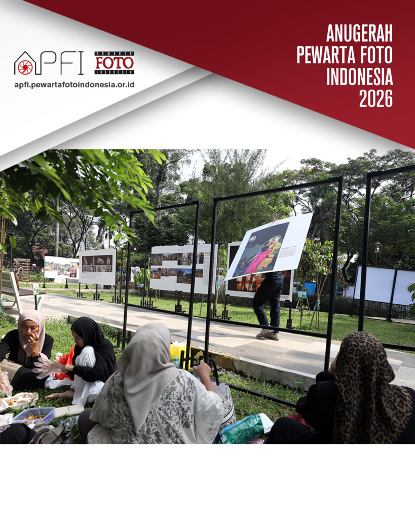 Sekelompok relawan perempuan berhijab duduk melingkar di atas rumput menyiapkan logistik konsumsi, berlatar belakang panitia yang mengangkat panel foto pameran.