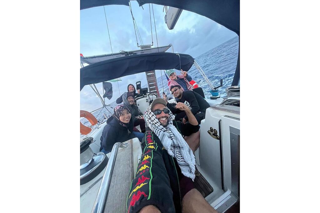 Foto bersama dari sudut pandang selfie memperlihatkan sekelompok jurnalis dan relawan Indonesia tersenyum di dalam kabin kemudi kapal layar di tengah perairan laut lepas.