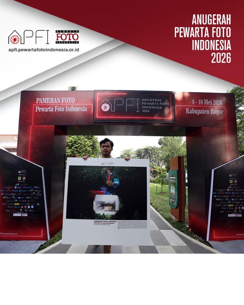 Seorang anggota panitia berjalan menggotong panel cetak foto berukuran besar berlabel "Nominasi Foto Tunggal Nature & Environment" melewati gerbang masuk utama pameran.