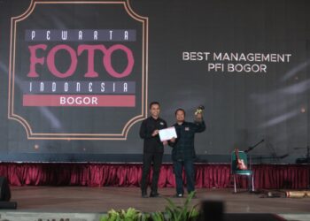 Ketua PFI Pusat Dwi Pambudi serahkan penghargaan ke PFI Bogor di atas panggung Anugerah Pewarta Foto Indonesia (APFI) 2026. Pria di sebelah kanan mengangkat trofi dan memegang piagam penghargaan dengan latar belakang layar LED bertuliskan "BEST MANAGEMENT PFI BOGOR"
