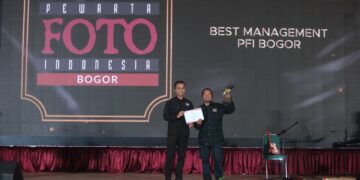 Ketua PFI Pusat Dwi Pambudi serahkan penghargaan ke PFI Bogor di atas panggung Anugerah Pewarta Foto Indonesia (APFI) 2026. Pria di sebelah kanan mengangkat trofi dan memegang piagam penghargaan dengan latar belakang layar LED bertuliskan "BEST MANAGEMENT PFI BOGOR"