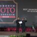 Ketua PFI Pusat Dwi Pambudi serahkan penghargaan ke PFI Bogor di atas panggung Anugerah Pewarta Foto Indonesia (APFI) 2026. Pria di sebelah kanan mengangkat trofi dan memegang piagam penghargaan dengan latar belakang layar LED bertuliskan "BEST MANAGEMENT PFI BOGOR"