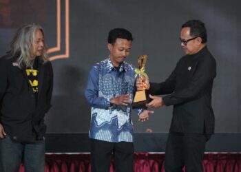 Fauzan (tengah) menerima trofi piala Alex dan Frans Mendur Trophy, penghargaan tertinggi Anugerah Pewarta Foto Indonesia (APFI) 2026, yang diserahkan oleh Wakil Menteri Dalam Negeri Bima Arya (kanan), didampingi oleh Koordinator Dewan Juri Oscar Matuloh (kiri) di atas panggung Auditorium Setda Kabupaten Bogor.