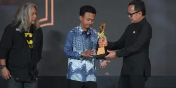 Fauzan (tengah) menerima trofi piala Alex dan Frans Mendur Trophy, penghargaan tertinggi Anugerah Pewarta Foto Indonesia (APFI) 2026, yang diserahkan oleh Wakil Menteri Dalam Negeri Bima Arya (kanan), didampingi oleh Koordinator Dewan Juri Oscar Matuloh (kiri) di atas panggung Auditorium Setda Kabupaten Bogor.