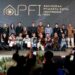 Momen penganugerahan gelar tertinggi Photo Of The Year APFI 2026 kepada Fauzan di atas panggung Auditorium Sekretariat Daerah Kabupaten Bogor, 8 Mei 2026. Fauzan berdiri di podium berbicara ke mikrofon sambil memegang bingkai foto besar karyanya yang monumental. Di sampingnya berdiri pria berkemeja batik memegang trofi. Backdrop LED besar di belakang mereka bertuliskan 'APFI 2026', 'Photo Of The Year', 'Fauzan', 'Demonstrasi Atas Tewasnya Ojol Yang Terlindas Rantis Brimob', dan logo PFI Pusat serta Pemkab Bogor.