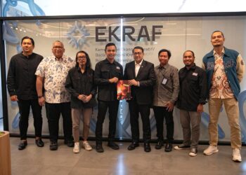 Delapan orang jajaran kementerian dan pengurus PFI berdiri sejajar memegang Buku Foto APFI 2026 bersama di depan dinding kaca bertuliskan EKRAF.