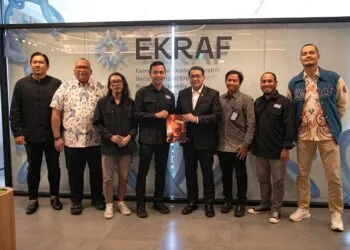 Delapan orang jajaran kementerian dan pengurus PFI berdiri sejajar memegang Buku Foto APFI 2026 bersama di depan dinding kaca bertuliskan EKRAF.