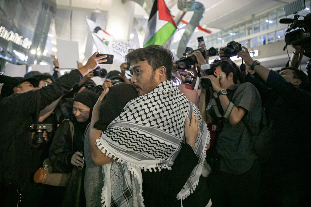 Foto emosional jurnalis Thoudy Badai memeluk erat istrinya di tengah kepungan kilatan kamera wartawan dan kibaran bendera Palestina di bandara.