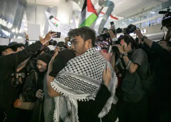 Foto emosional jurnalis Thoudy Badai memeluk erat istrinya di tengah kepungan kilatan kamera wartawan dan kibaran bendera Palestina di bandara.
