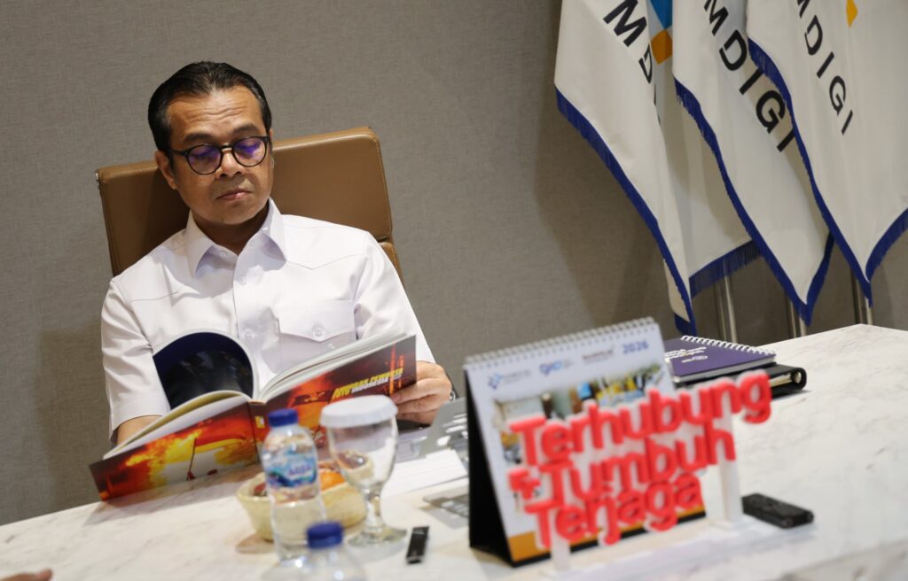 Wakil Menteri Komunikasi dan Digital Nezar Patria duduk serius di meja kerja sembari membuka lembar demi lembar halaman Buku Foto APFI 2026.