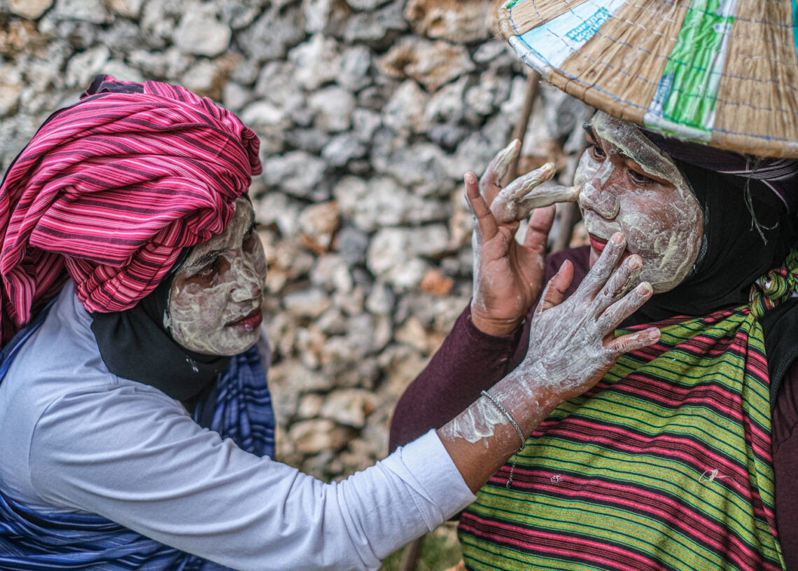 Seorang peserta membantu rekannya mengoleskan bedak basah ke wajah sebelum mengikuti tradisi Hekente di Wakatobi, Sulawesi Tenggara